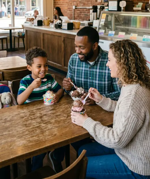 A foster family of two parents and their young son sharing ice cream together at a cozy neighborhood ice cream shop