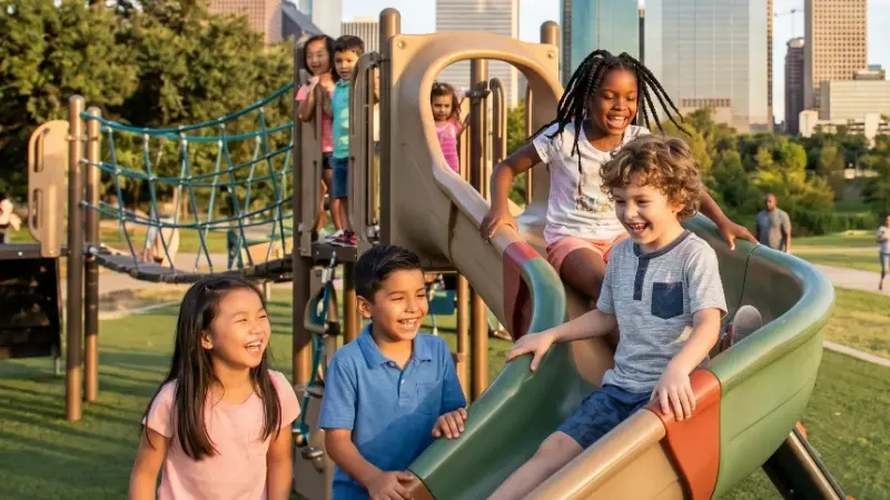 A group of laughing children playing on a slide and playground structure in a Houston park